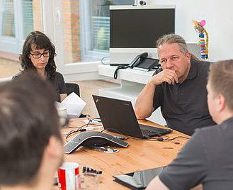 company meeting with employees sitting around a conference table with laptops and notes