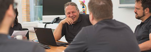 company meeting with employees sitting around a conference table with laptops and notes